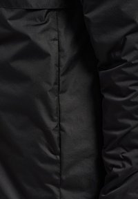 Schwarze isolierte Jacke mit einer strukturierten Oberfläche, dezentem Glanz und sichtbaren Nähten entlang der Nähte; taillenlanger Schnitt ohne Hardware-Details.