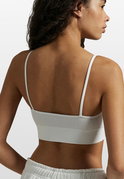 Bílý krátký top na tenká ramínka s žebrovanou strukturou a hladkou tkaninou. Nastavitelný střih s jednoduchým, bezešvým designem.