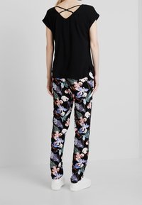 Top nero a maniche corte con schiena incrociata, abbinato a pantaloni neri con motivo floreale featuring fiori rosa e blu, scarpe bianche.