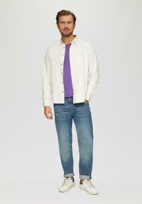 Weiß karierte Langarmhemd über einem lila T-Shirt, kombiniert mit hellblauen Jeans und weißen Sneakers. Einfaches, lässiges Outfit.