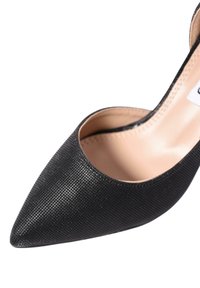 Scarpa nera con punta appuntita realizzata in materiale testurizzato con design a bassa scollatura. La soletta è beige e il tacco è a stiletto.