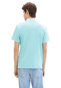 Polo bleu clair à manches courtes, avec un col blanc et des finitions blanches contrastantes, fabriqué en tissu lisse. Vue de dos.