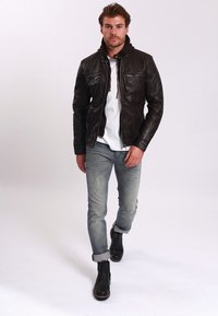 Hnědá kožená bunda s zipovými kapsami, přepsaná přes bílou košili. Nosit s světle modrými džíny a černými kotníkovými botami.