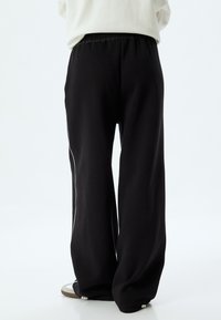 Zwarte relaxed-fit broeken van zachte stof, met een elastische tailleband en witte zijkanten, met een losse pasvorm.