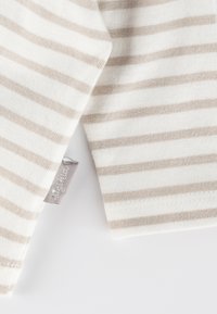 Top in tessuto leggero con righe beige orizzontali su uno sfondo bianco, dotato di una piccola etichetta sulla cucitura laterale.