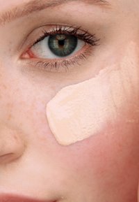 Se aplica una base líquida en un tono beige claro sobre la piel, fusionándose con una textura suave sobre un cutis con pecas.