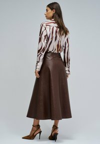 Falda midi marrón con estampado de cocodrilo y cintura alta, combinada con una blusa de manga larga con rayas abstractas en marrón y crema.
