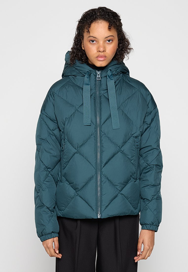 Turkusowa kurtka puchowa z kapturem, z zamkiem błyskawicznym, diamentowym pikowaniem i dwoma bocznymi kieszeniami. Jej materiał ma gładką, lekką teksturę.