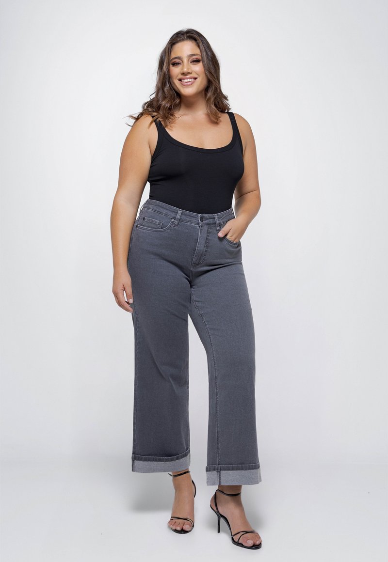 Zwarte bodysuit gecombineerd met grijze hoge taille wijde jeans, met een opgerolde zoom. Model staat zelfverzekerd, draagt een paar zwarte sandalen met banden.