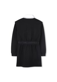 Svart kjole med hvit krage, lange ermer og innsvingt midje med elastisk bånd med merke. Glatt stoff og knelang design.