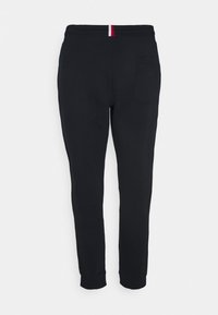 Schwarze Jogginghosen aus weichem Material. Sie verfügen über eine schmale Passform, einen elastischen Bund mit einem roten und weißen Streifen sowie eine einzelne Gesäßtasche.