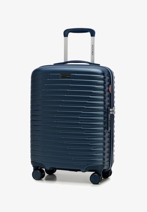 Valigia rigida blu navy con texture a righe, manico telescopico argentato e ruote multidirezionali. Presenta una zip e un accento con logo.