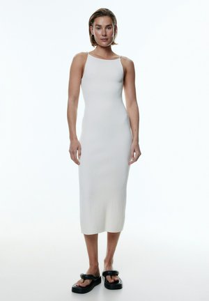 Weißes, geripptes Midikleid mit dünnen Trägern, figurbetonter Silhouette und glatter Textur. Kombiniert mit dicken schwarzen Plateausandalen.