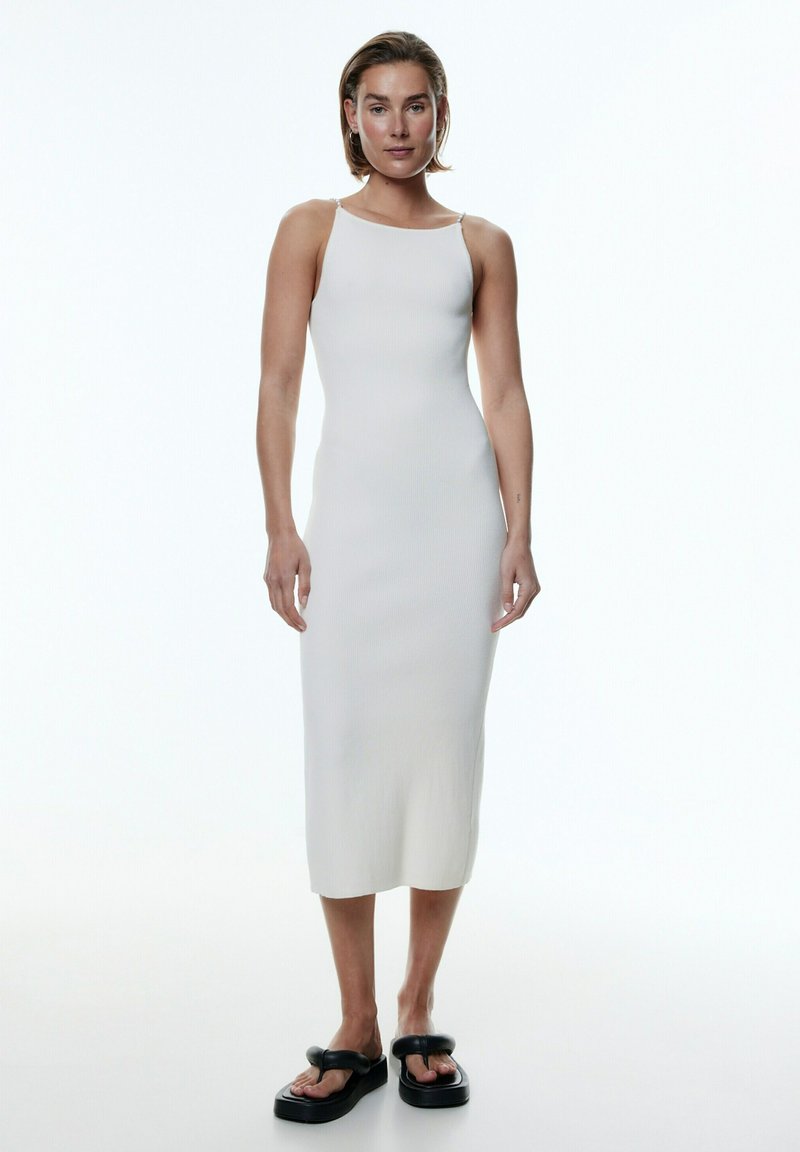 Weißes, geripptes Midikleid mit dünnen Trägern, figurbetonter Silhouette und glatter Textur. Kombiniert mit dicken schwarzen Plateausandalen.
