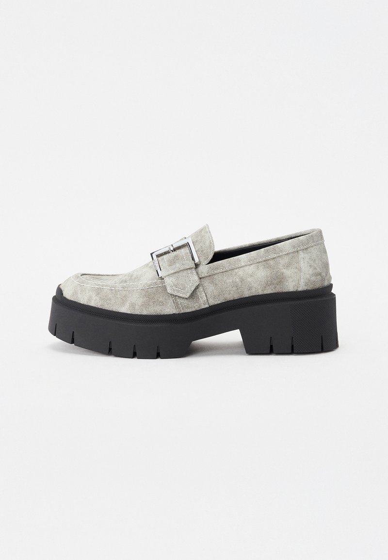 Grå ruskinds loafers med en kraftig sort platformsål, prydet med en dekorativ sølvspænde og et rundt tådesign.