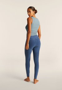 Leggings in denim blu aderenti con vita alta e tasche posteriori, abbinati a un top senza maniche azzurro chiaro. Texture liscia, design minimalista.