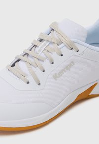 Chaussure de sport blanche avec une tige en mesh texturé, des lacets gris clair et une semelle en caoutchouc orange, arborant un motif triangulaire subtil et un logo.