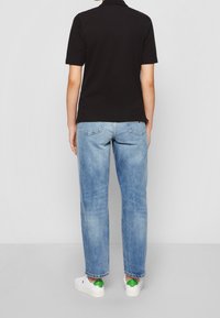 Schwarzes Poloshirt mit kurzen Ärmeln, hellblaue weite Jeans und weiße Turnschuhe mit grünen Akzenten. Das Outfit zeichnet sich durch eine lässige, entspannte Passform aus.