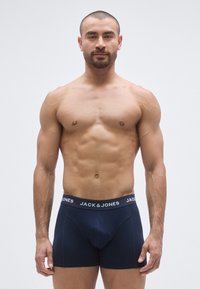 Tumši zili bokseršorti ar zīmola elastīgu jostu, izgatavoti no mīksta auduma, ar piegulošu dizainu un izteiktām šuvju detaļām.