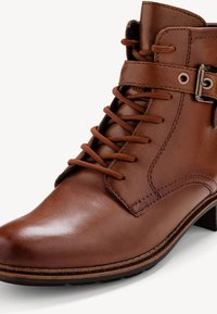 Botte de cheville en cuir marron avec un bout arrondi, un système de laçage et un accent de boucle en métal. Texture lisse et profil de talon bas.