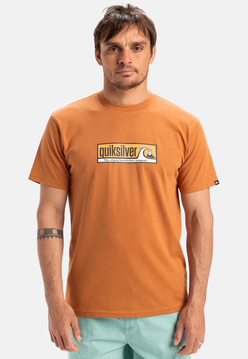 Camiseta de manga corta naranja de algodón, con un logotipo de Quiksilver y un gráfico de montaña y ola en blanco y negro. Textura suave, cuello redondo.