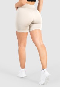 Beige high-waisted shorts met een gladde textuur, een aangesloten ontwerp en contrasterende afwerking. Draagt met witte sport schoenen en sokken.