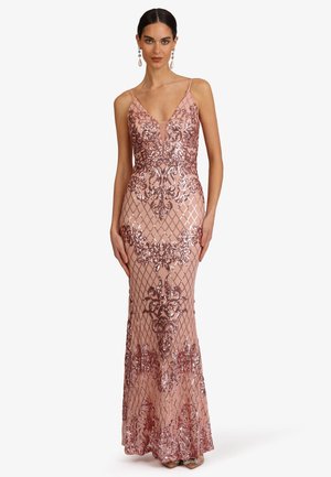 Frau trägt ein ärmelloses, bodenlanges Kleid in Blush mit rosegoldenen Paillettenblumen- und Gittermustern, tiefem V-Ausschnitt und hängenden Ohrringen.