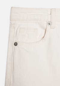 Tissu en denim blanc avec une surface texturée, comportant une petite poche avant, un bouton en métal et des détails de couture contrastés.