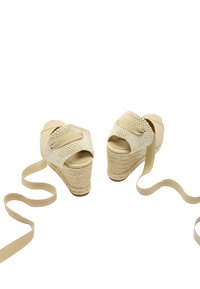 Beżowe sandały na koturnie z plecionym jutasowym obcasem i tekstylną górą. Posiadają szeroką opaskę i długie materiałowe paski.