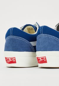 Paire de baskets en toile bleue et en daim avec semelles blanches et logos rouges "Off The Wall" sur le talon arrière affichant le détail de la marque.