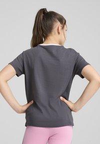 Camiseta gris de mangas cortas con un cuello redondo y ribete blanco, hecha de una suave mezcla de algodón. Se lleva con leggings de color rosa claro.