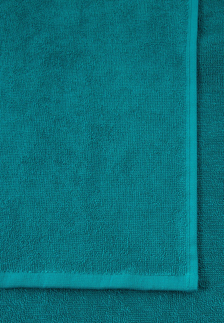 Asciugamano in cotone color teal con superficie strutturata. I bordi sono rifiniti con un trim coordinato. Due asciugamani impilati con cuciture visibili.