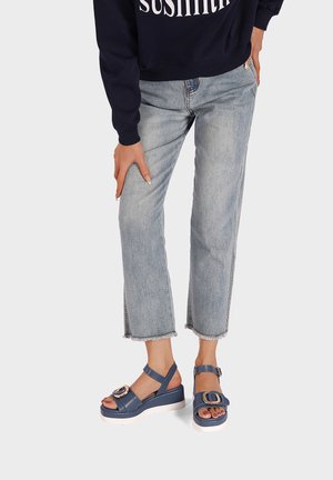 Sandali con platform blu navy e cinturino alla caviglia, con un accento circolare, abbinati a pantaloni di denim chiari con orli sfrangiati.