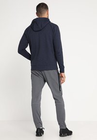 Sudadera con capucha azul marino de acabado texturizado y pantalones deportivos grises con rayas laterales. Ambas prendas son ajustadas para mayor comodidad.