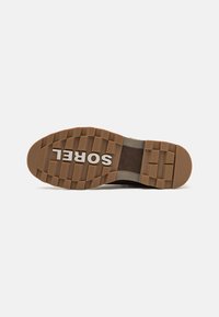 Suela de zapato marrón con textura de goma, que presenta un agarre con patrón. Nombre de la marca "SOREL" en blanco, ubicado de manera central en la suela.