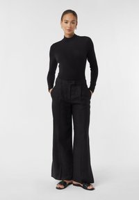 Zwarte lange mouwen top, gecombineerd met hoge taille, wijde zwarte broek. Glad stof en gestroomlijnd ontwerp, aangevuld met platte sandalen.