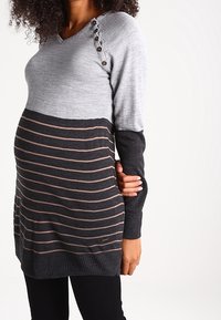 Sweter ciążowy z szarym górnym fragmentem i ciemnoszarym korpusem w paski z różowymi paskami. Dekolt w kształcie litery V i guziki na ramieniu.