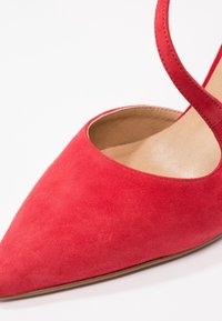Chaussure plate pour femme en daim rouge à bout pointu avec une fine bride de cheville et une doublure intérieure beige.