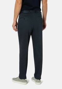 Donkerblauwe, gestructureerde broek met een rechte pasvorm, voorzien van twee achterzakken en een gladde tailleband. Gecombineerd met lichtgrijze sneakers.