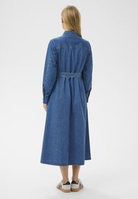 Denim midi-jurk met een ceintuuroptie, lange mouwen en een kraaghalslijn. Heeft een rechte zoom en zichtbare stiksels. Gemaakt in combinatie met casual schoenen.