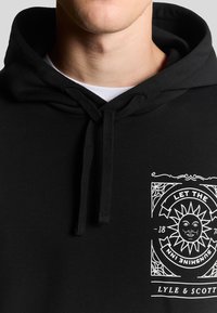 Felpa nera in cotone, con una grafica frontale raffigurante un sole e testo. Il tessuto è liscio e presenta un cappuccio regolabile con cordino.