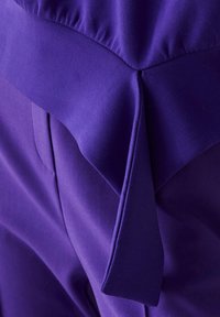 Gros plan sur un tissu violet avec des plis structurés et des plis nets créant un motif géométrique en couches.