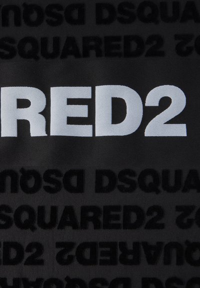 Μαύρο ύφασμα με έντονο, λευκό κείμενο "RED2" και επαναλαμβανόμενο ανάγλυφο μαύρο "DSQUARED". Οι υφές αντιπαραβάλλονται μεταξύ των χρωμάτων.