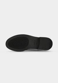 Μαύρη σόλα παπουτσιού με υφή πρόσοψης και ανάγλυφο λογότυπο Geox κοντά στην καμάρα, σε απλό φωτεινό φόντο.