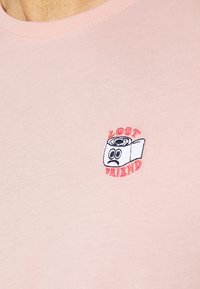 Světle růžové tričko vyrobené z měkké látky, s malou vyšitou grafikou karikatury pásky a textem "ZTRACENÝ PŘÍTEL."