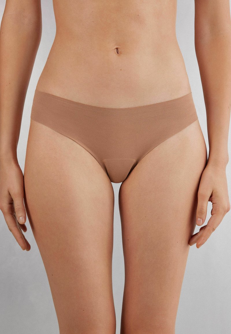 Naadloze, lichtbruine bikinislips met een gladde textuur en minimale tailleband. Ontworpen voor comfort en een lage pasvorm.