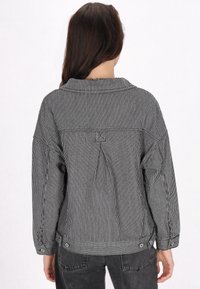 Svart- och vitrandig jacka med skjortkrage, sänkta axlar och knäppta ärmslut. Har en detalj vid bakstycket och en avslappnad passform.