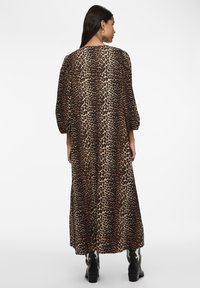 Abito maxi con stampa leopardata e maniche a sbuffo, realizzato in morbido tessuto. Presenta una schiena aperta. Indossato con stivali neri con tacco. Sfondo neutro.