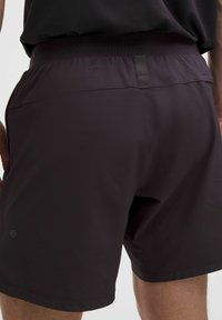 Miestne športové šortky v tmavofialovej látke, s textúrovaným povrchom, elastickým pásom a malým reflexným logom na dolnej ľavej strane.