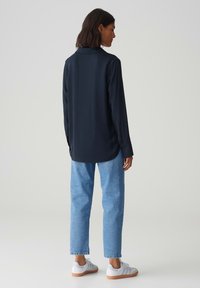 Maglietta a maniche lunghe blu navy con colletto, abbinata a jeans dritti azzurri e sneaker bianche con suola in gomma. Design semplice e pulito.